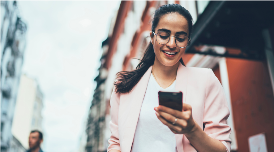 woman smiling while walking and looking at her phone